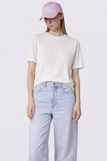 Person wearing a white t-shirt, light blue jeans, and a pink cap on a plain background
