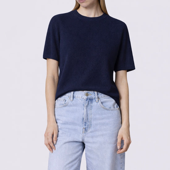 Person wearing a navy t-shirt and cap with light blue jeans on a white background