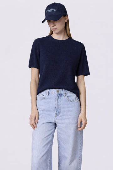 Person wearing a navy t-shirt and cap with light blue jeans on a white background