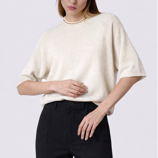 Woman wearing a white oversized sweater and black pants on a plain background