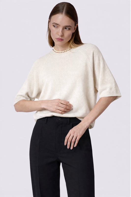 Woman wearing a white oversized sweater and black pants on a plain background