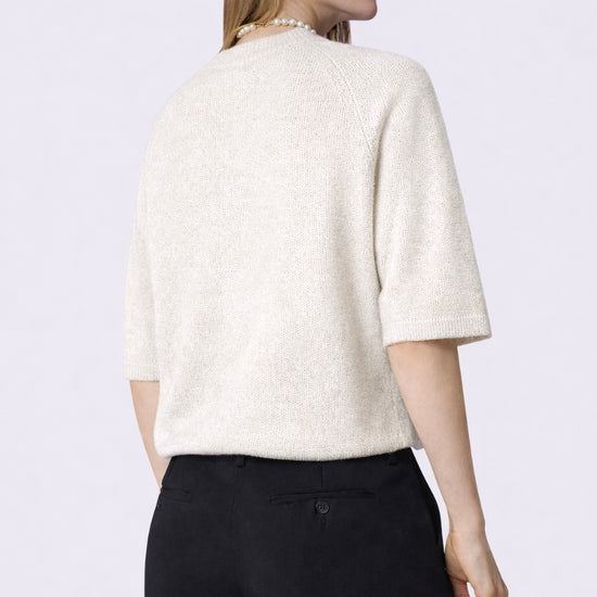 Woman wearing a white textured top and black pants on a light purple background