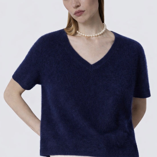 Woman wearing a navy blue sweater and white pants against a plain background