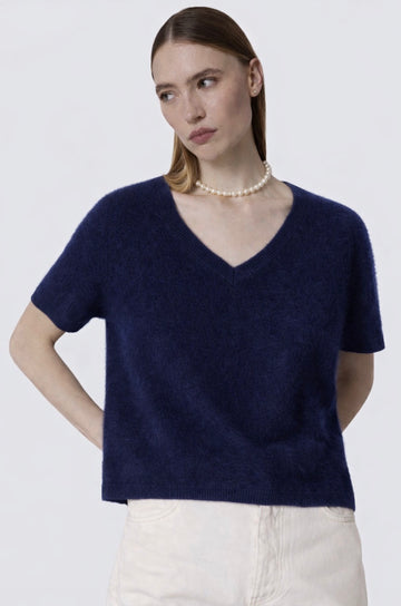 Woman wearing a navy blue sweater and white pants against a plain background