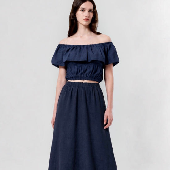 Woman wearing a navy blue off-shoulder top and long skirt on a light gray background