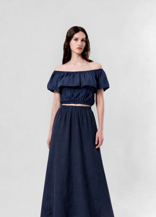 Woman wearing a navy blue off-shoulder top and long skirt on a light gray background