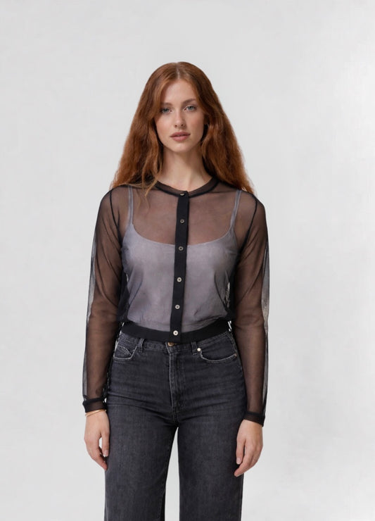 Woman wearing a sheer black blouse over a gray top with dark jeans on a white background