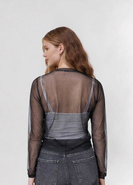 Woman wearing a sheer long-sleeve top over a gray shirt with dark jeans on a white background