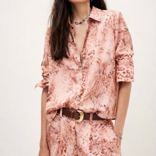 Woman wearing a pink floral shirt and pants with a belt, standing against a white background