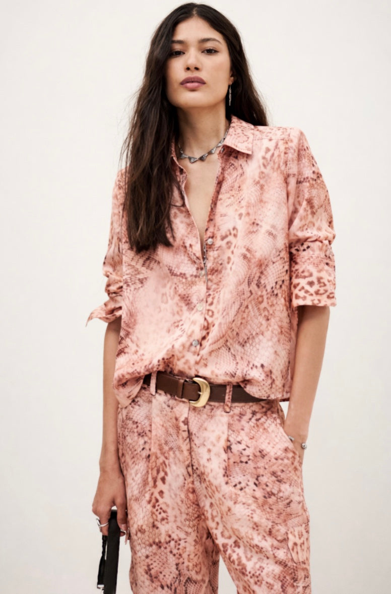 Woman wearing a pink floral shirt and pants with a belt, standing against a white background