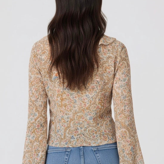 Woman wearing a patterned blouse and jeans on a plain background