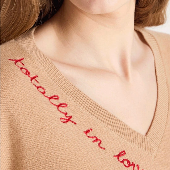 Woman wearing a beige sweater with text and blue jeans on a white background