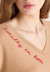 Woman wearing a beige sweater with text and blue jeans on a white background