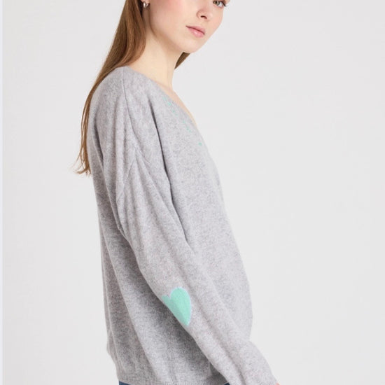Woman wearing a gray sweater with heart patterns on a plain background