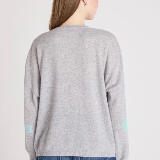 Woman wearing a gray sweater with heart patterns on a plain background
