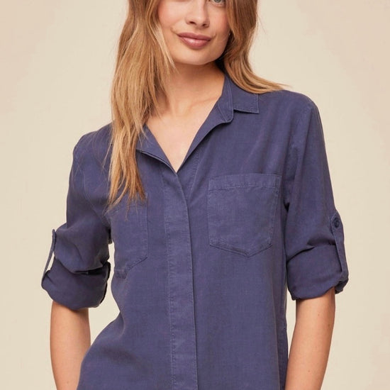 Woman wearing a blue shirt with rolled-up sleeves against a beige background