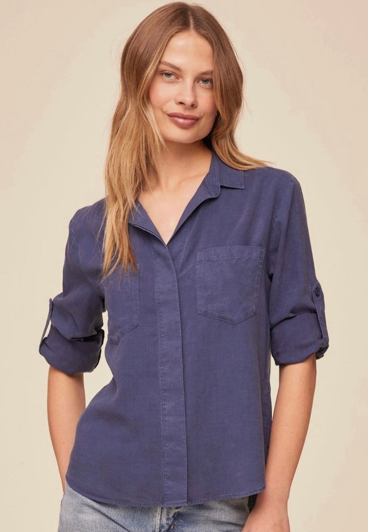 Woman wearing a blue shirt with rolled-up sleeves against a beige background