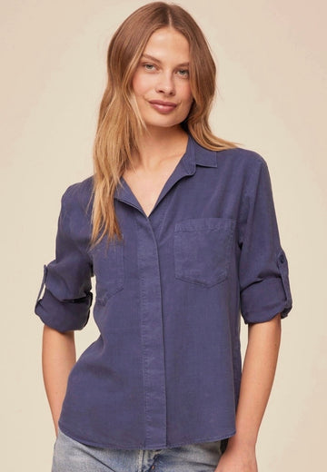 Woman wearing a blue shirt with rolled-up sleeves against a beige background