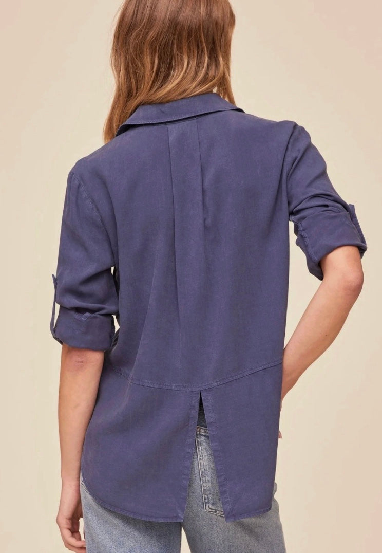 Woman wearing a blue shirt with rolled-up sleeves against a beige background