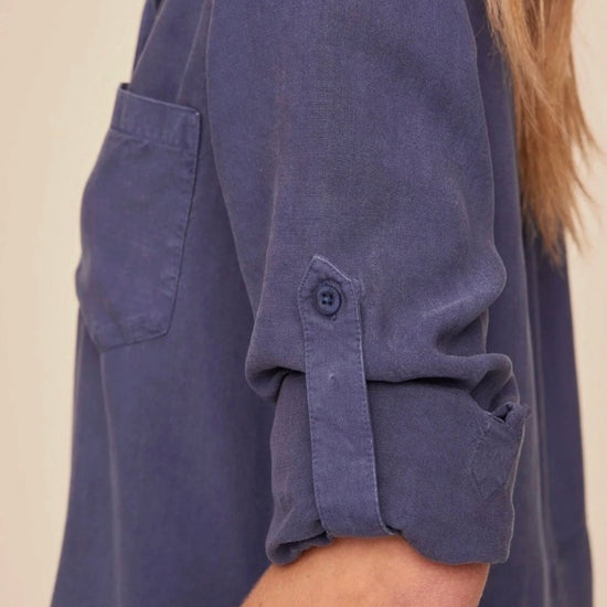 Woman wearing a blue shirt with rolled-up sleeves against a beige background