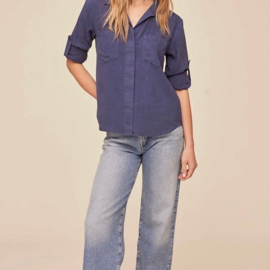 Woman wearing a blue shirt with rolled-up sleeves against a beige background