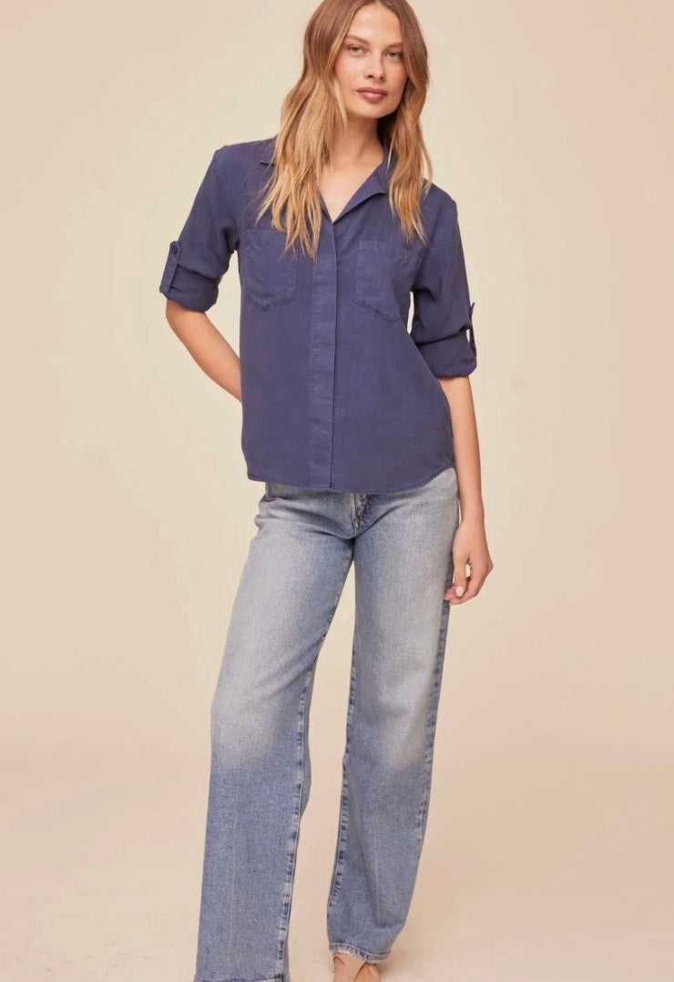 Woman wearing a blue shirt with rolled-up sleeves against a beige background