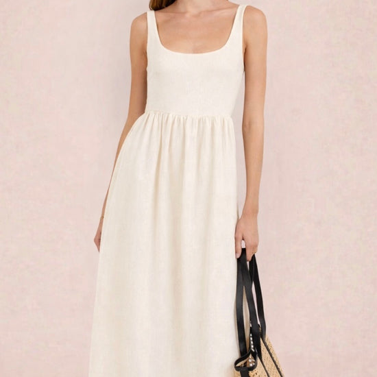 Woman wearing a white dress holding a black and beige handbag against a light pink background