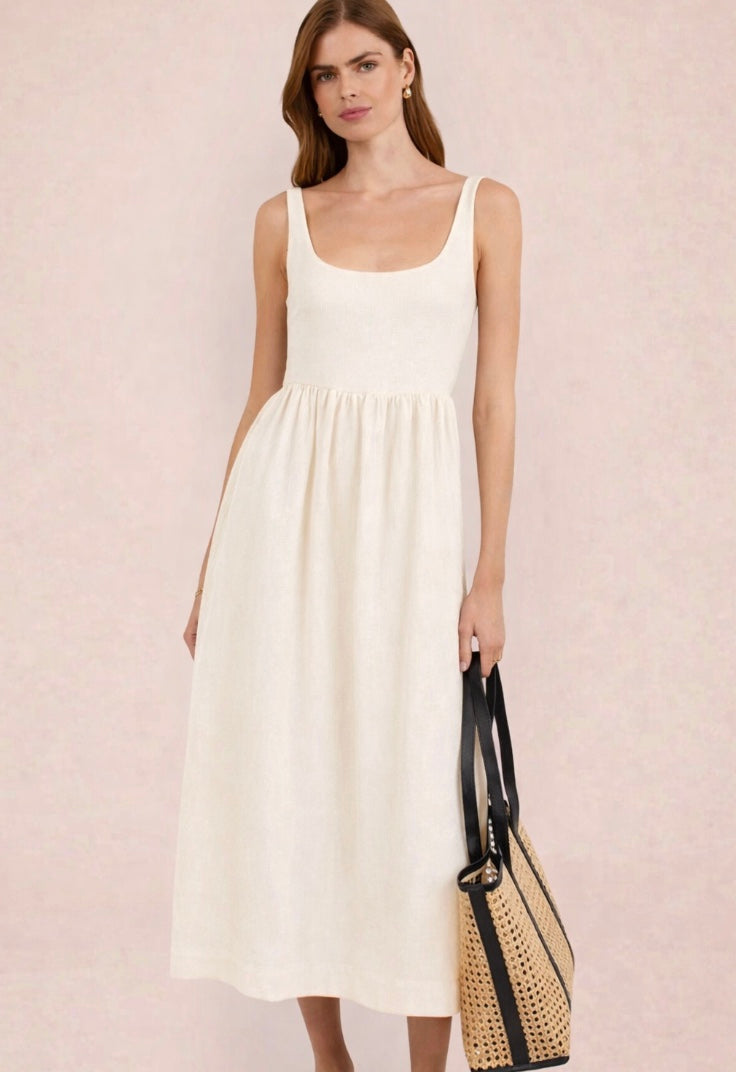 Woman wearing a white dress holding a black and beige handbag against a light pink background