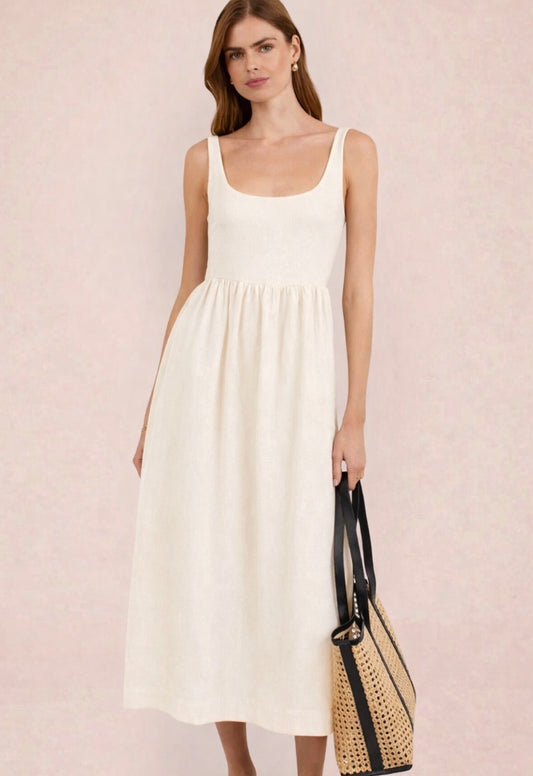 Woman wearing a white dress holding a black and beige handbag against a light pink background