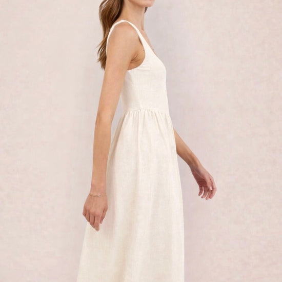 Woman wearing a white dress holding a black and beige handbag against a light pink background