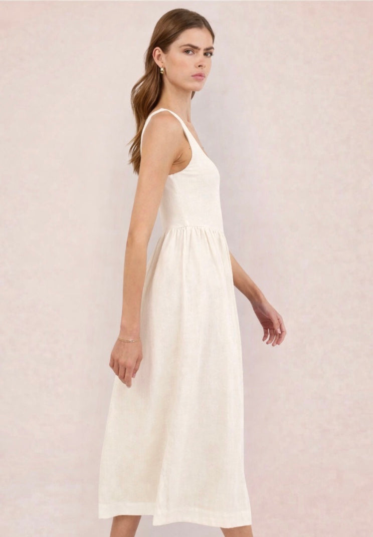 Woman wearing a white dress holding a black and beige handbag against a light pink background