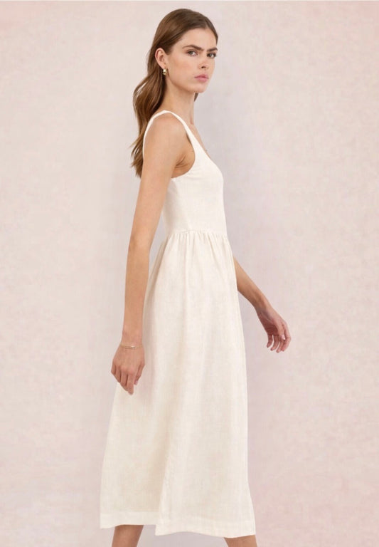 Woman wearing a white dress holding a black and beige handbag against a light pink background