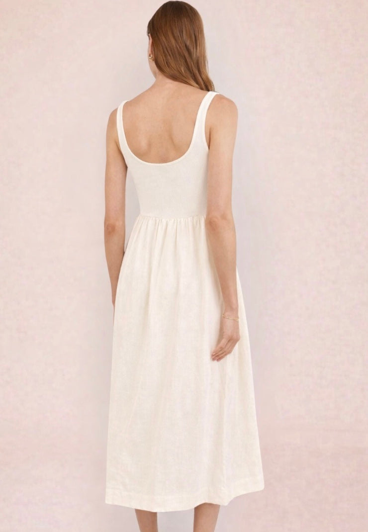 Woman wearing a white dress holding a black and beige handbag against a light pink background