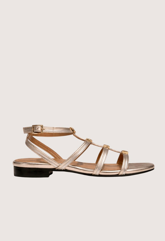 Gold sandal with a black sole on a light gray background