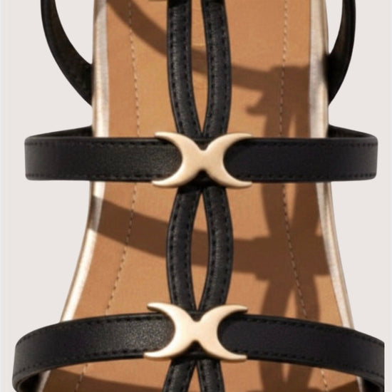 Close-up of black strappy sandals with gold crescent moon buckles on a beige background