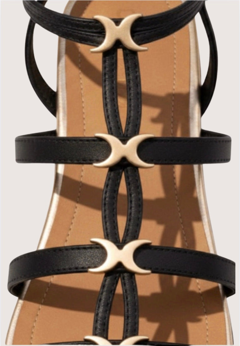 Close-up of black strappy sandals with gold crescent moon buckles on a beige background