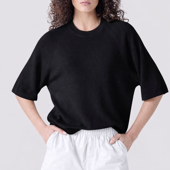 Person wearing a black oversized t-shirt and white shorts on a plain background