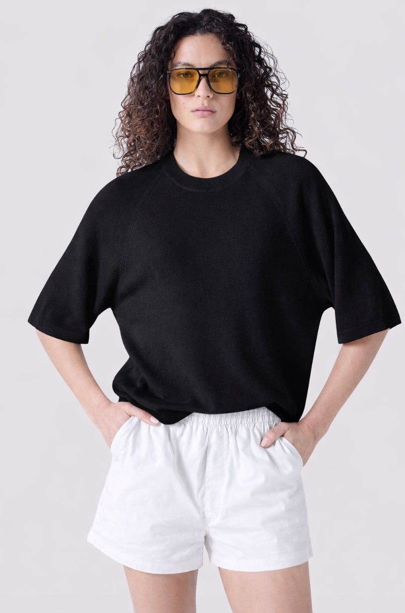 Person wearing a black oversized t-shirt and white shorts on a plain background