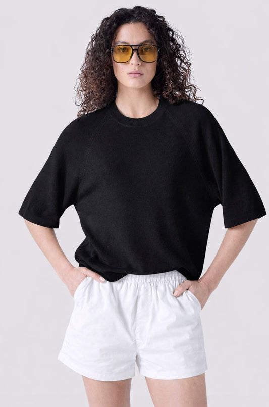 Person wearing a black oversized t-shirt and white shorts on a plain background