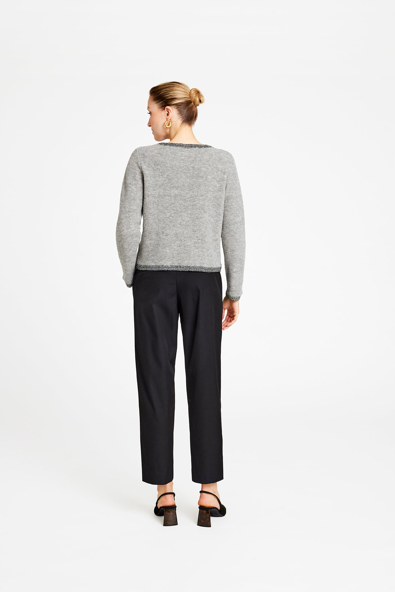 Person wearing a gray sweater and black pants on a white background