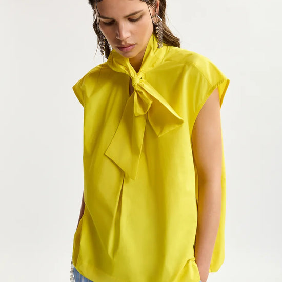 Woman wearing a yellow blouse with a bow detail on a white background