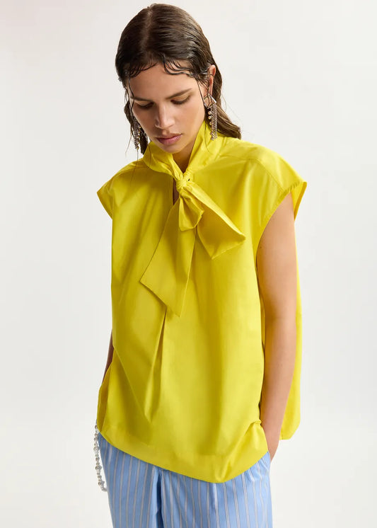 Woman wearing a yellow blouse with a bow detail on a white background