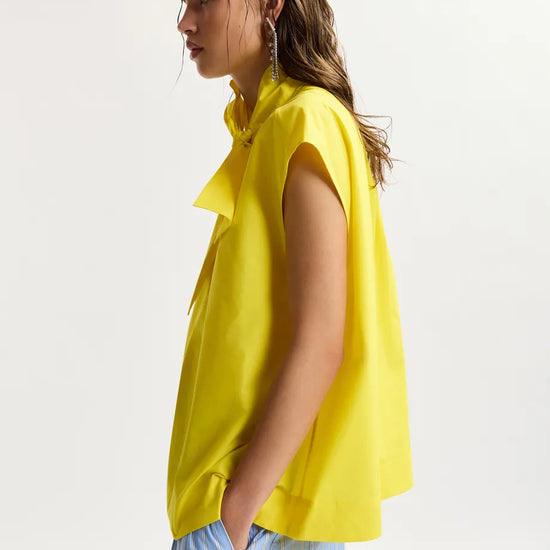 Woman wearing a yellow sleeveless top with a plain background