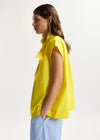Woman wearing a yellow sleeveless top with a plain background