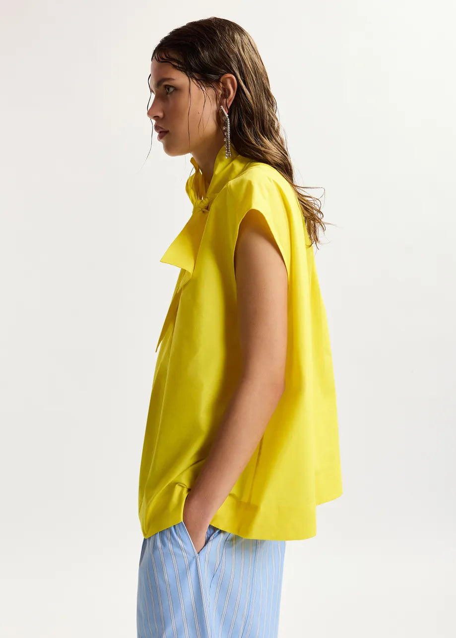 Woman wearing a yellow sleeveless top with a plain background