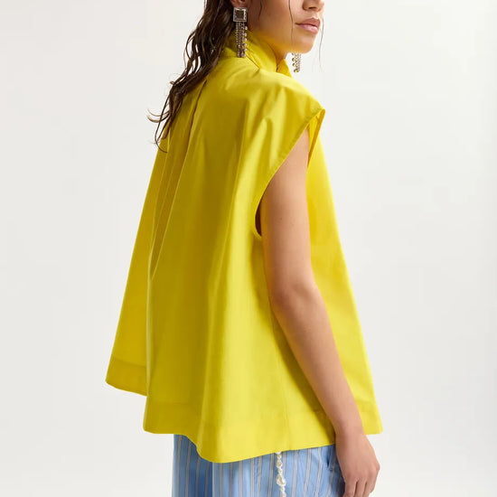 Woman wearing a yellow sleeveless top with blue striped pants on a white background