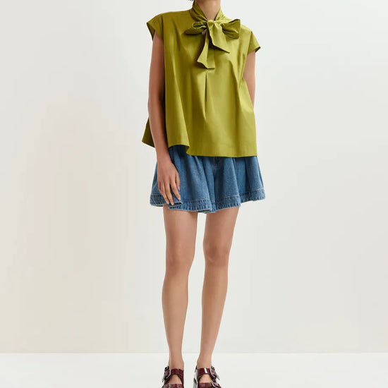 Woman wearing a green blouse with a bow and denim skirt on a white background