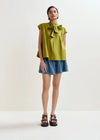 Woman wearing a green blouse with a bow and denim skirt on a white background