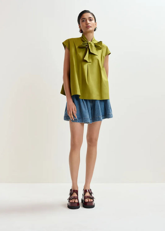 Woman wearing a green blouse with a bow and denim skirt on a white background