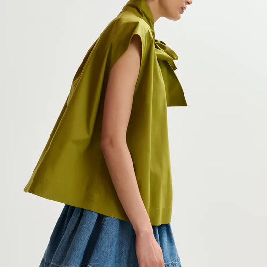 Woman wearing a green sleeveless top with a bow detail and a denim skirt on a white background